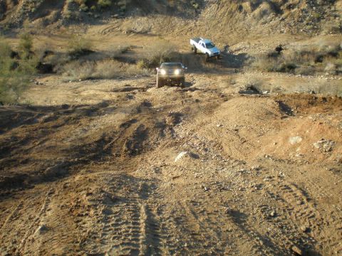 1991 Ford Bronco - Two trucks navigate a challenging off-road terrain with steep inclines and loose dirt.