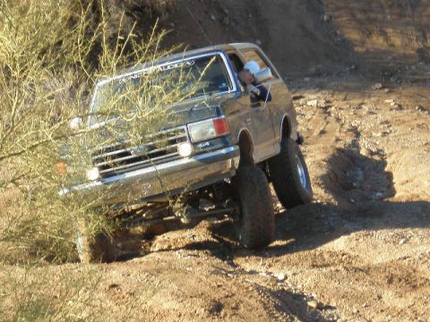 1991 Ford Bronco - A dark gray Ford Bronco navigates a steep, dusty incline during an off-road excursion.