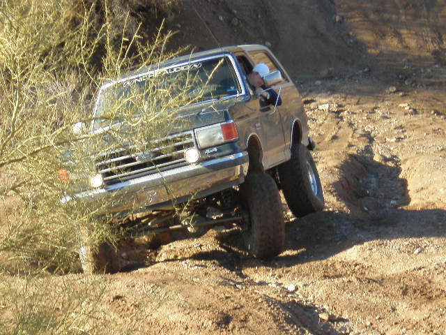 Dark gray Ford Bronco off-roading on a dirt hill, front driver's side tire visible