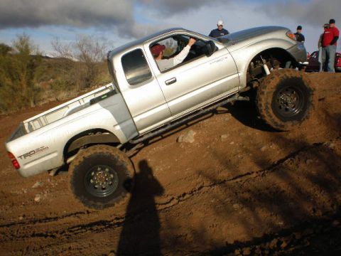 1991 Ford Bronco - A lifted Toyota Tacoma TRD Off-Road navigates a steep dirt incline with onlookers present onlookers present onlookers present onlookers pre…