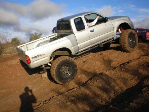 1991 Ford Bronco - A silver pickup truck navigates a dirt incline with a second vehicle visible in the background.