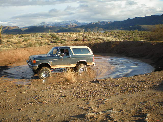 1991 Ford Bronco driving through a muddy water hole in a desert landscape