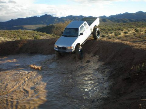 1991 Ford Bronco - Pickup truck navigating a muddy water obstacle in a dry, hilly landscape.