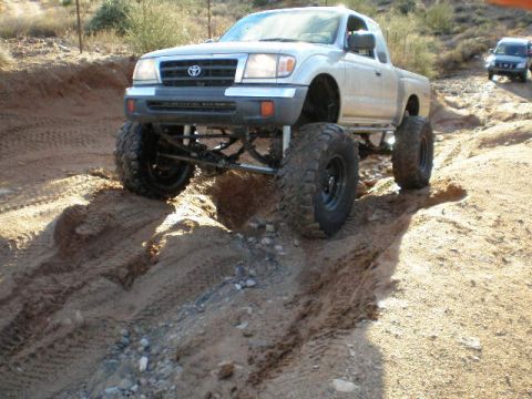 1991 Ford Bronco - A modified Toyota Tacoma navigates a challenging dirt path with large off-road tires.