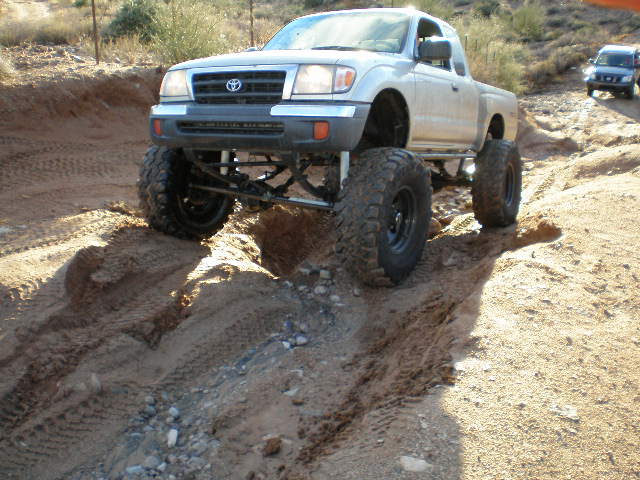 Lifted Toyota Tacoma truck driving on a dirt trail. Another SUV is visible in the background