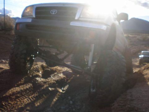 1991 Ford Bronco - A lifted Toyota Tacoma navigates a muddy, off-road trail under a bright sun.