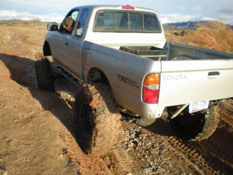 1991 Ford Bronco - A silver Toyota pickup truck navigates a muddy, off-road trail with large, aggressive tires.