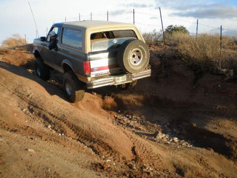 1991 Ford Bronco - A 1991 Ford Bronco navigates a steep, dusty trail under a partly cloudy sky.