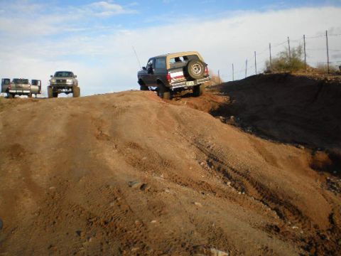 1991 Ford Bronco - Multiple trucks and SUVs navigate a dirt hill under a blue sky.