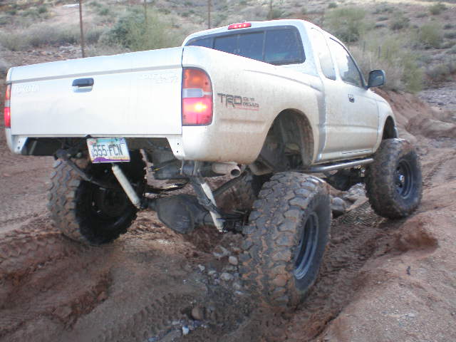Silver Toyota Tacoma pickup truck with large off-road tires and suspension lift, seen from rear