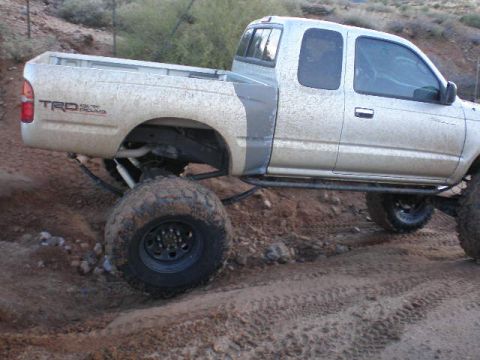 1991 Ford Bronco - A silver pickup truck, modified for off-road use with large tires and TRD badging, navigates a dirt path.