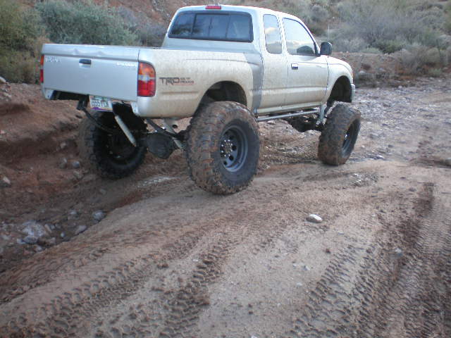 Lifted 1998 Toyota Tacoma pickup truck with large off-road tires on a dirt trail