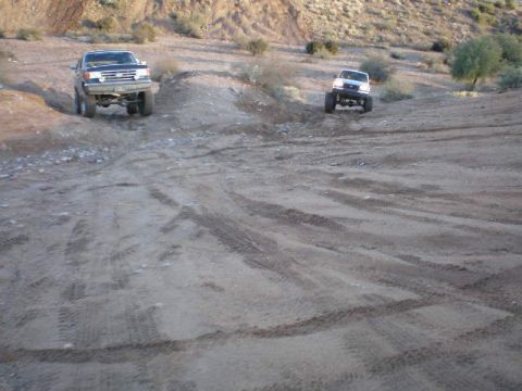 1991 Ford Bronco - Two trucks navigate a dusty, off-road trail in a dry, hilly landscape.