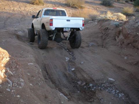 1991 Ford Bronco - Pickup truck navigates a challenging off-road path in a desert landscape.