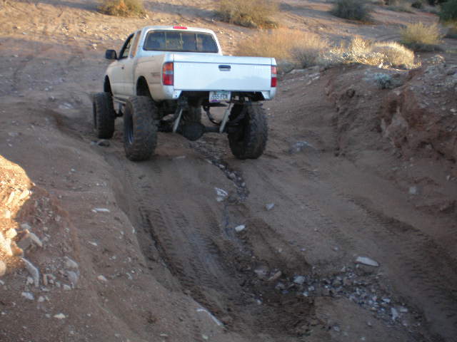 White pickup truck with large tires driving on a dirt trail