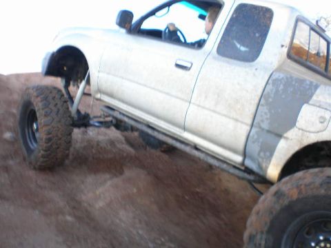 1991 Ford Bronco - A white pickup truck navigates a steep, muddy incline during an off-road excursion.