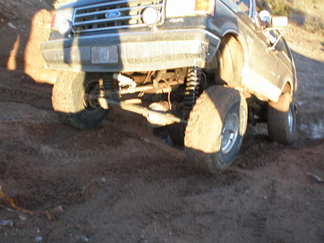 Front driver's side of a lifted 1991 Ford Bronco off-roading on a dirt trail
