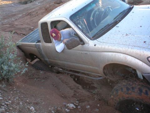 1991 Ford Bronco - A silver pickup truck is stuck in a muddy ditch, with the driver looking down from the open window.