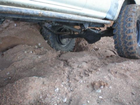 1991 Ford Bronco - Undercarriage view of an off-road vehicle with its rear tire partially submerged in loose dirt.