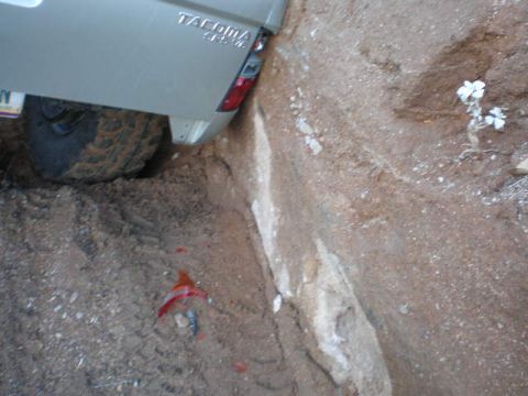 1991 Ford Bronco - A Toyota Tacoma truck is stuck in a narrow dirt ditch, with its rear tire wedged against the side.