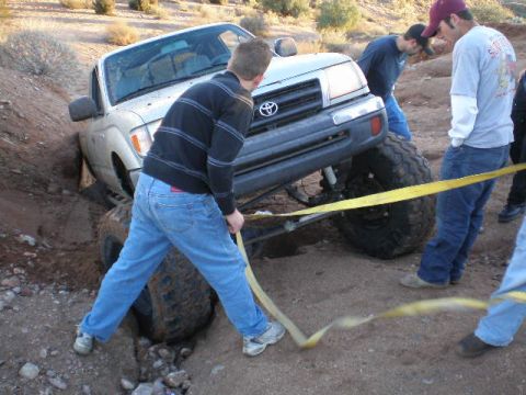 1991 Ford Bronco - A group of people are attempting to free a stuck Toyota Tacoma from a muddy ditch using a tow strap.