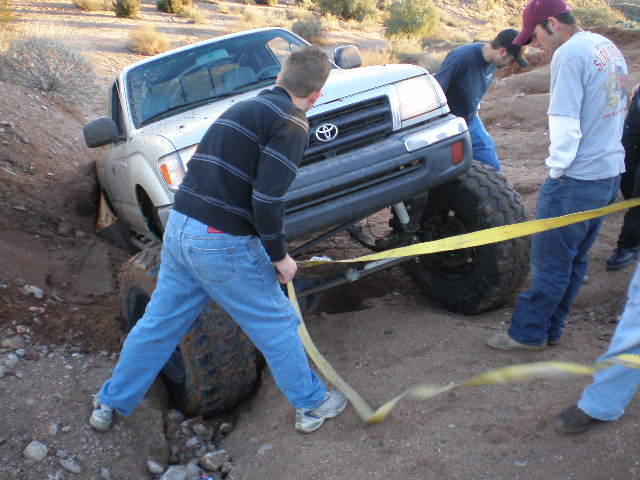 Truck stuck in a ditch, people trying to pull it out with a yellow strap