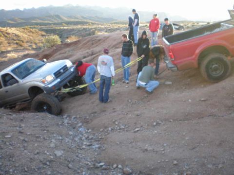 1991 Ford Bronco - People attempt to free a silver pickup truck stuck in a ditch with the help of a red truck.