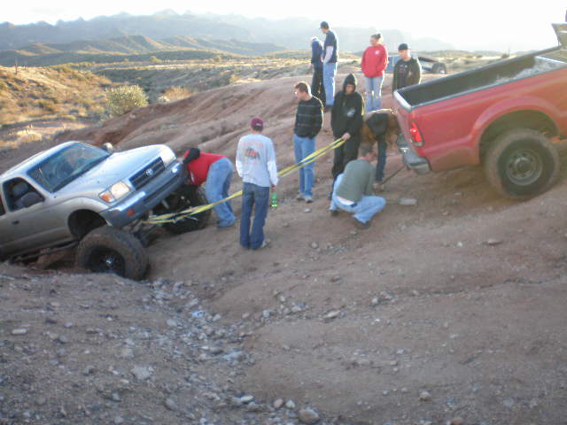 Silver pickup truck stuck in dirt, being pulled by a red truck