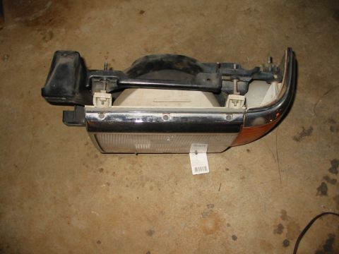 1988 Ford Bronco - A single vehicle headlight assembly is shown, detached from the vehicle, resting on a concrete floor.