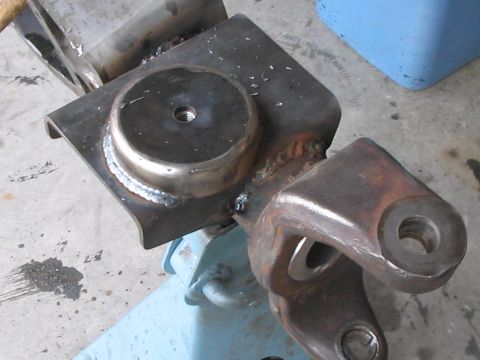 1991 Ford Bronco - A close-up view of a custom-welded metal part, likely for a vehicle suspension, resting on a blue jack.