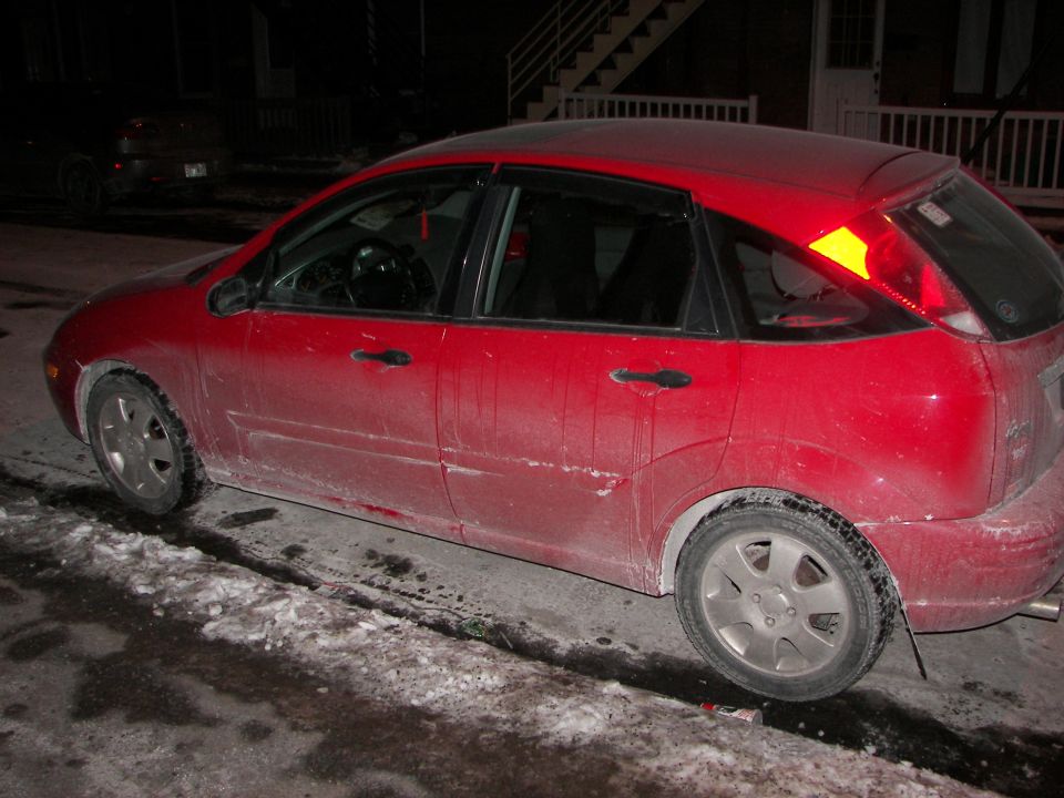 Red Ford Focus hatchback parked on a snowy street at night. Another car is visible in the background