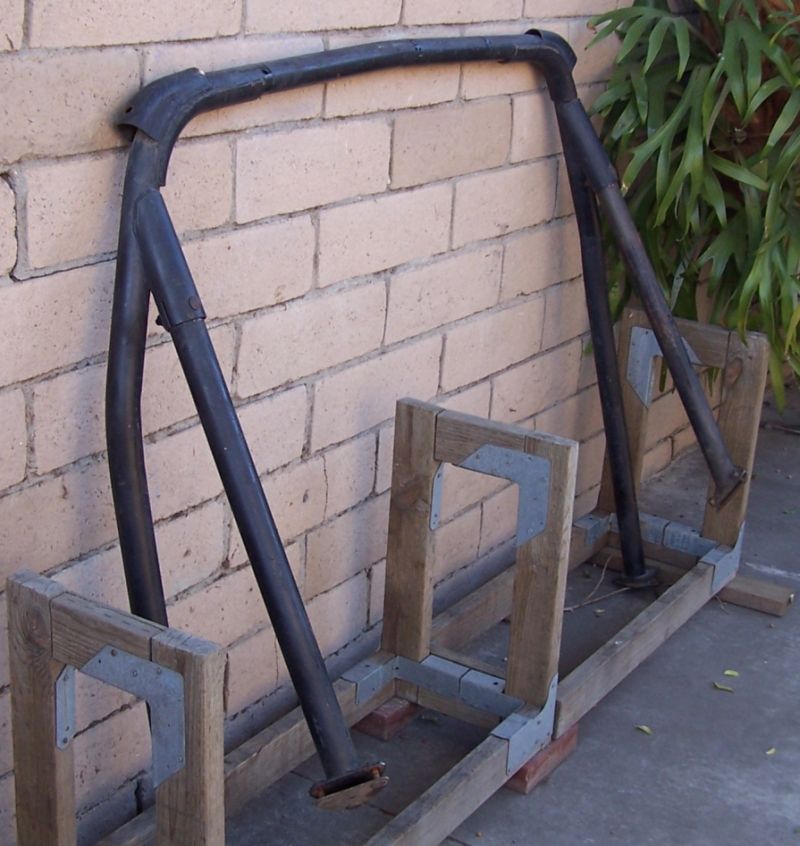 Black tubular roll bar hoop resting on a wooden jig against a cinder-block wall