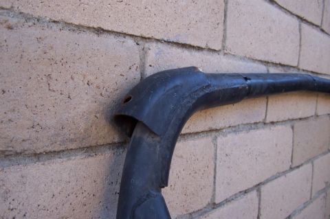 1990 Ford Bronco - A section of a black roll bar with damaged plastic trim is shown against a brick wall.