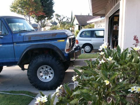 1978 Ford Bronco - A blue pickup truck is parked in front of a garage, with a white minivan visible in the background.