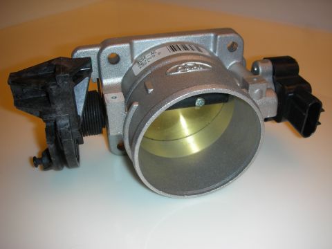 1998 Ford Crown Victoria - aluminum throttle body with a brass bore and a black sensor attached, shown at an angle on a tan surface.