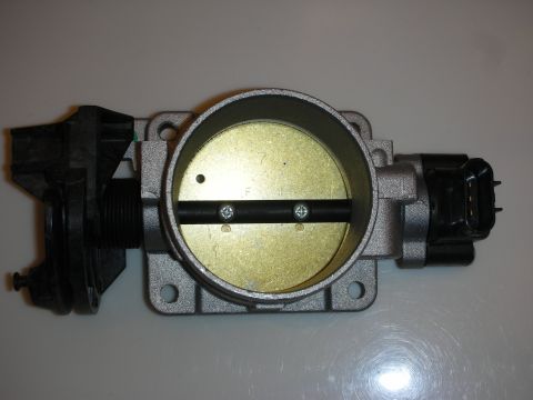 1998 Ford Crown Victoria - Overhead view of an aluminum throttle body showing the brass bore, butterfly plate and an attached black sensor.