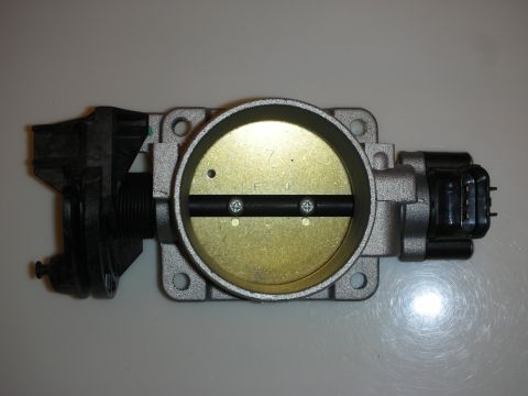 1998 Ford Crown Victoria - Aluminum throttle body viewed from above with closed butterfly plate, mounting holes and a side electrical connector.