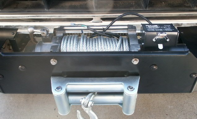 Black electric winch with steel cable and roller fairlead mounted behind a bumper