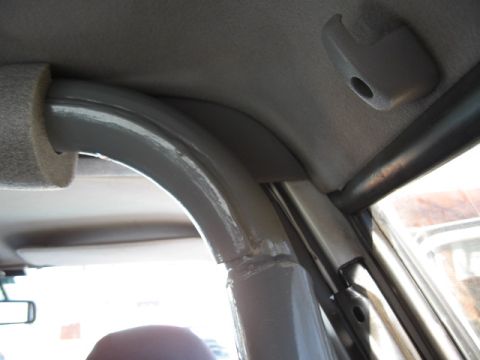1994 Ford Bronco - Interior close-up looking up at a custom welded roll cage in a truck cab, where a painted A-pillar hoop and a black side bar run tight agai…