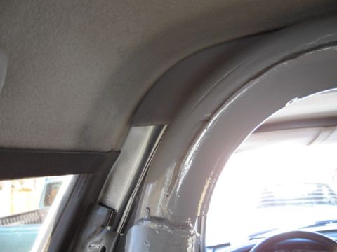 1994 Ford Bronco - Interior close-up looking up at the driver's-side A-pillar and windshield header of a truck, showing gray cloth headliner meeting a bare pa…