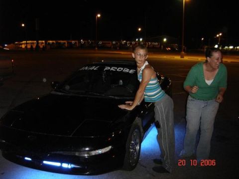1995 Ford Probe - A black coupe with blue underglow is parked at night, with two people standing nearby. Text on the windshield reads "ANAL PROBE".