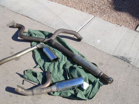 1996 Ford Probe - Several exhaust system components, including pipes and mufflers with chrome tips, are arranged on a green tarp.
