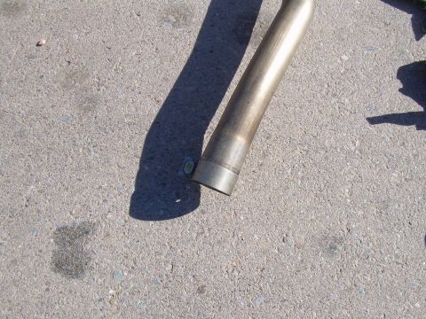 1996 Ford Probe - A section of an exhaust pipe lies on a concrete surface, casting a long shadow.