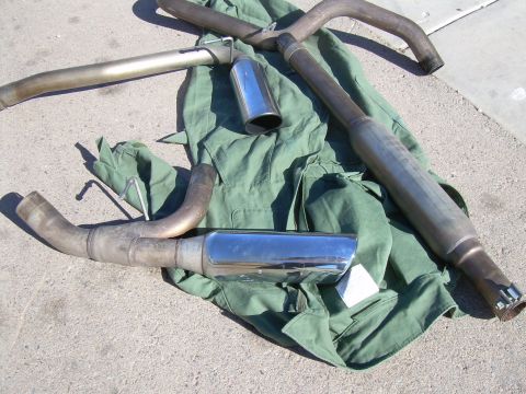 1996 Ford Probe - Several exhaust system components, including mufflers and chrome tips, are displayed on a piece of green fabric on the ground.