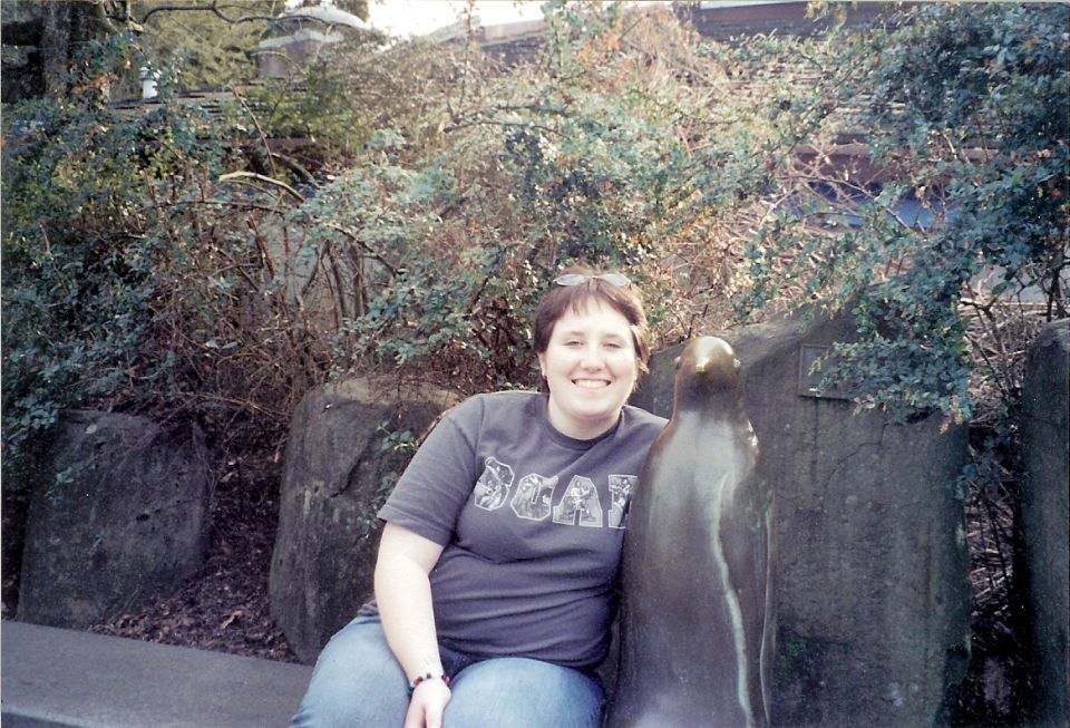 Person seated outdoors beside a bronze sea lion statue