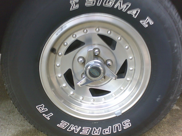 Close-up of a chrome wheel with a three-pronged spinner and a black tire with white lettering reading "SUPREME TR" and "SIGMA"