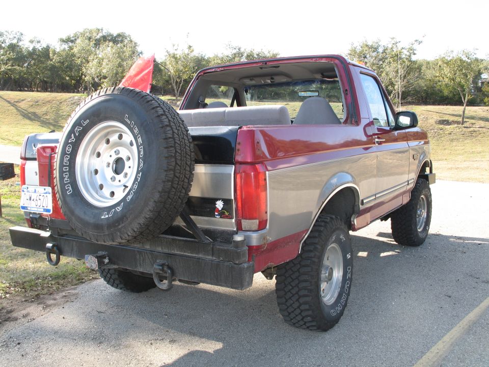 Two-tone maroon/silver full-size Ford Bronco, top off, rear spare, parked on a rural road.