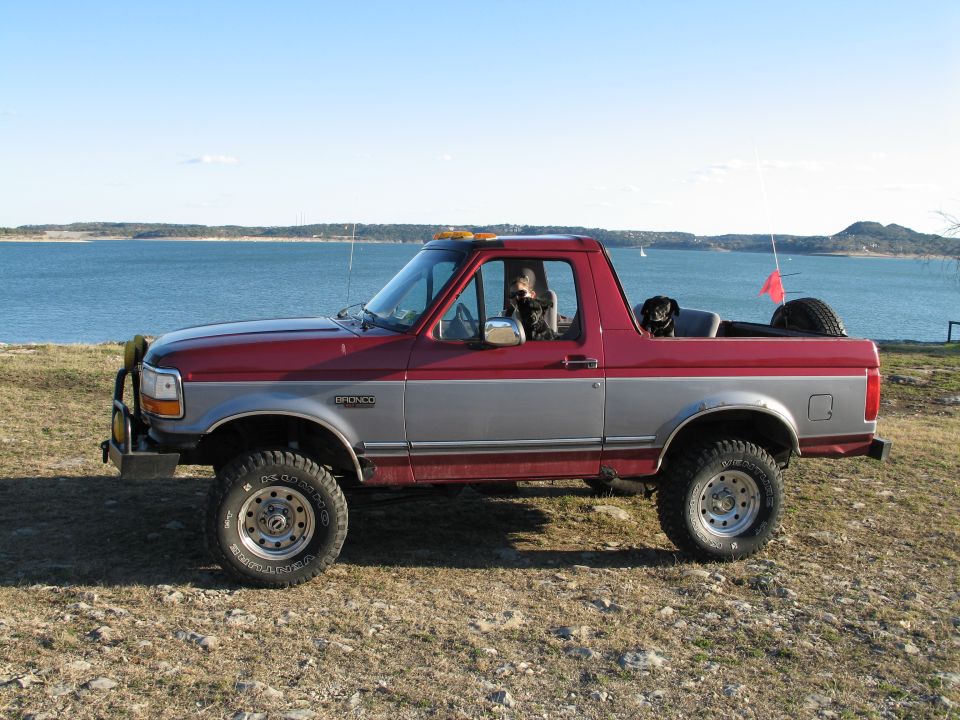 Lifted red and silver Ford Bronco with top removed parked on a rocky lakeshore