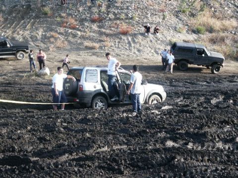 1978 Ford Bronco - Multiple vehicles and people are stuck in a muddy area after an apparent off-road excursion.