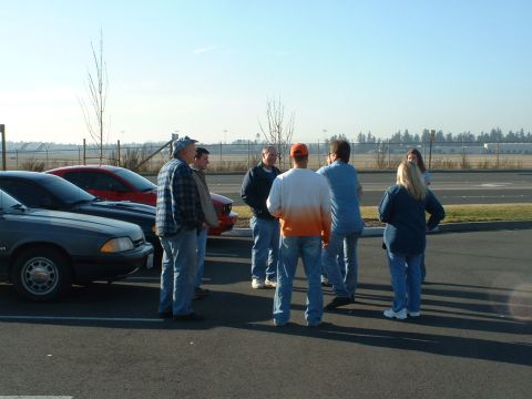 2000 Ford Crown Victoria - A group of people stand around two Ford Mustang hatchbacks in a parking lot.